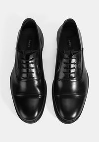 Zwarte leren schoenen met een gladde afwerking, voorzien van een ronde neus, veters en een subtiel ontwerp. De zool is getextureerd voor grip.