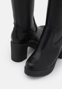 Botines negros de cuero liso, con punta redondeada, tacón cuadrado y mínimos detalles de costura en el lateral.