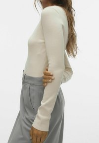 Långärmad, ljusbeige figurnära topp i texturerad tyg, kombinerad med höga, ljusgrå byxor med sidofickor.