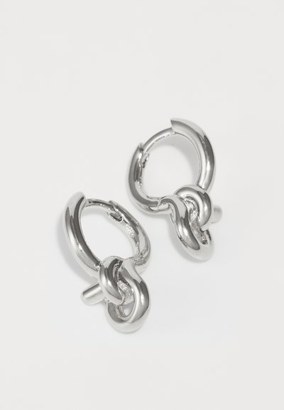 Silver hoop earrings featuring interlocking design elements, smooth texture, and a shiny finish. Each earring has a stud attachment.