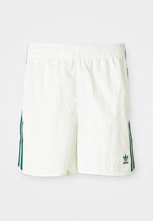 Białe szorty z elastycznym paskiem w talii, z zielonymi pionowymi paskami po bokach i wyszywanym logo Adidas w kolorze zielonym.