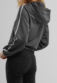 Gray cropped hoodie with a hood, featuring white side stripes and elastic cuffs. Paired with black high-waisted jeans.