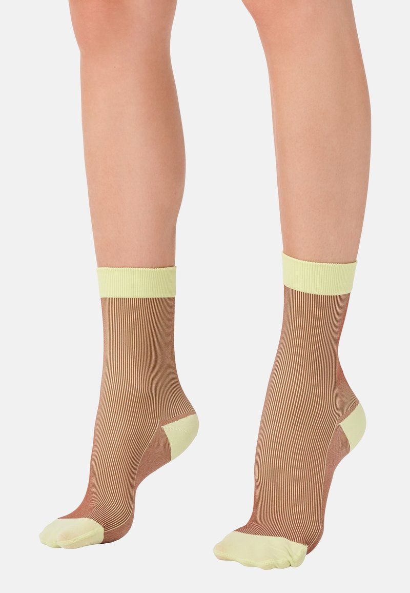 Gestreifte Knöchelsocken mit einem hellgelben Bündchen und Zehen, die einen durchsichtigen braunen Körper mit feinen vertikalen Linien und einer verstärkten Ferse aufweisen.
