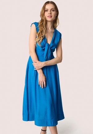 Robe sans manches bleue avec un détail à nouer au niveau du col, longueur genoux, présentant une texture douce et une silhouette évasée.