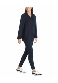 Marineblouse met een v-hals en gerimpelde mouwen, gecombineerd met donkere skinny jeans en zwart-witte sneakers, wat zorgt voor een casual outfit.