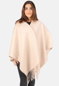 Beiger Poncho aus weichem Stoff, mit dreieckiger Form, asymmetrischem Saum und langen Fransen an den unteren Kanten.