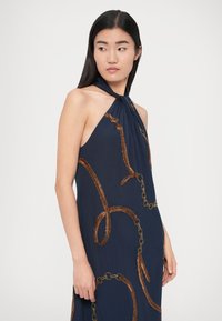 Rochie halter bleumarin, cu broderie elaborată asemănătoare unui lanț de bronz, material fluid și decolteu drapat pentru o siluetă elegantă.