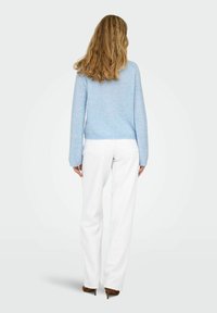 Pull tricoté bleu clair avec manches texturées et à motifs, associé à un pantalon blanc à jambes larges et des chaussures à talons marron.