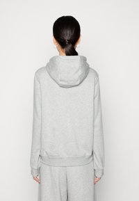 Siv sweatshirt s kapuco, izdelan iz mehkega materiala z dolgimi rokavi in ribanim robom. Ima sproščen kroj in minimalističen dizajn.