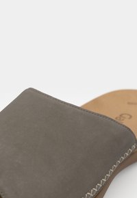 Sandale à glisser en suède gris avec une texture lisse, présentant des coutures contrastées sur le dessus et une semelle intérieure beige.