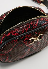 Borsa con motivo in pelle di serpente rossa e nera, con cerniera e dettagli in oro. Superficie testurizzata, forma arrotondata, tracolla singola regolabile. Tasca interna visibile.