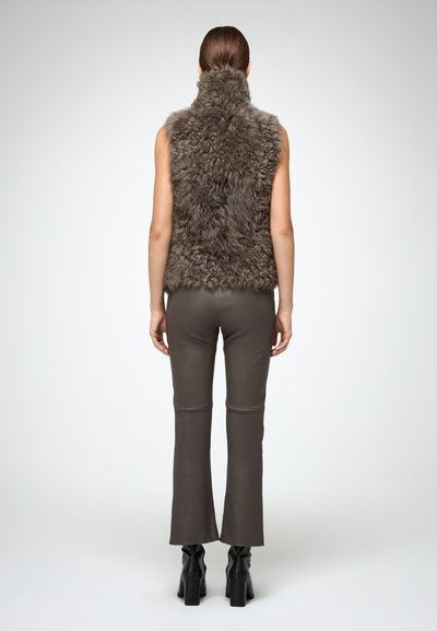 Gilet in finta pelliccia grigio scuro con un colletto alto, abbinato a pantaloni in pelle marrone attillati. Presenta un tessuto texturizzato e una linea dei pantaloni a zampa.