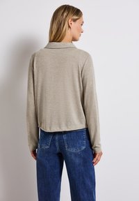 Ljust beige långärmad topp med krage, ribbad textur och en kort design, kombinerad med hög midja blå denimjeans.