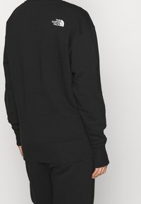 Schwarzer Sweatshirt aus Baumwolle mit gerippten Bündchen und Saum, mit einem weißen Logo auf der Rückseite. Einfaches, locker sitzendes Design.