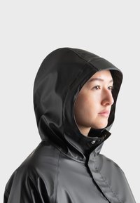 Chaqueta negra impermeable con capucha, fabricada en un material brillante y suave, con cierre de cremallera y un corte relajado, diseñada para protegerse de las inclemencias del tiempo.
