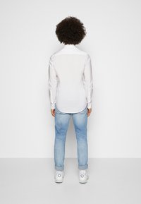 Camicia bianca a maniche lunghe con colletto aperto, abbinata a jeans azzurri chiari e sneakers bianche. Tessuto morbido con polsini buttoned.