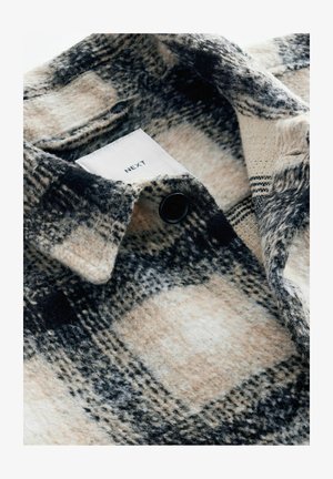 Camicetta di flanella a quadri in beige, nero e bianco. Presenta un bottone nero, una texture morbida e un'etichetta con la scritta "NEXT" visibile.