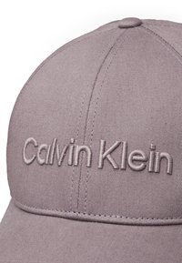Svetlo vijolična bejzbol kapa iz mešanice bombaža. Ima vezeno "Calvin Klein" logo v skladni barvi. Vidni so šivi.