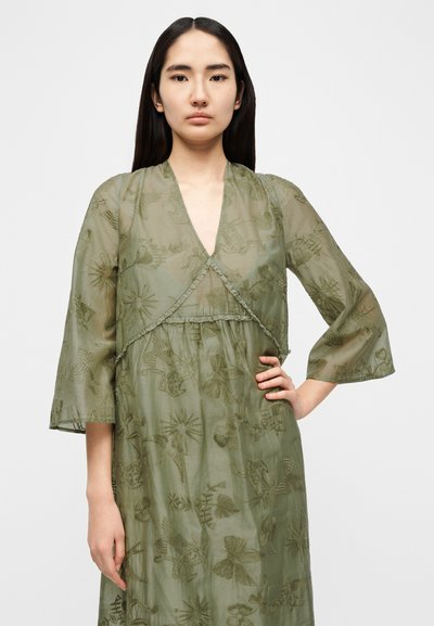 Φόρεμα σε ελιά πράσινο, διαφανές, με μακριά μανίκια και κέντημα με λουλούδια, v-λαιμόκοψη και ελαφρώς σούρες στη μέση με άνετη γραμμή.