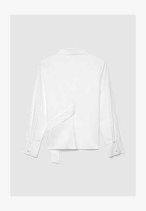 Camicia bianca a maniche lunghe con colletto classico. Presenta un design unico sul retro con un nodo laterale. Tessuto liscio e lavorato, con polsini abbottonati.