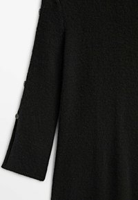 Manche longue noire texturée avec trois petits boutons ronds le long du côté extérieur de la manche, près du poignet.