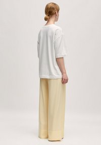 Witte oversized katoenen T-shirt met korte mouwen, gecombineerd met lichtgele wijde broek, met een gladde textuur en eenvoudig ontwerp.