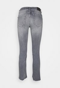 Zadní pohled na šedé džíny z denimu se dvěma zadními kapsami a detailními surovými lemy na jednobarevném pozadí.