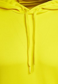 Sudadera amarilla con una textura suave, con capucha ajustable y puntas doradas en los cordones. Sin patrones o gráficos visibles.