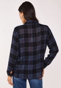 Camicia flanella a quadri nera e blu con maniche lunghe, polsini abbottonati e vestibilità rilassata, caratterizzata da un colletto e dettagli con spacco laterale.