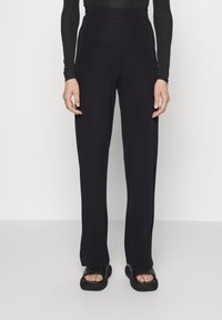 Černé, volné kalhoty se širokými nohavicemi a elastickým pasem. Vyrobené z měkké, elastické tkaniny. Spárovány s plochými černými sandály.