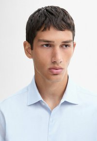 Light blue button-up shirt with a spread collar, featuring a smooth texture and understated design. No notable patterns or accents visible.