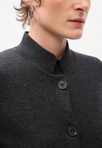 Chaqueta de punto texturizada en gris oscuro con cuello alzado, que presenta dos botones negros en la parte delantera. Vista en primer plano que resalta el detalle de la tela.