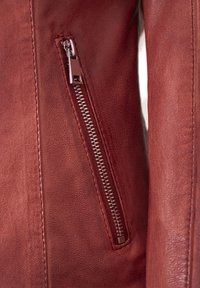 Rote Lederjacke mit einer Metallschnellverschluss-Tasche, strukturiertem Finish und klaren Linien für einen taillierten Schnitt. Nahaufnahme des Reißverschlussdetails.