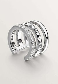 Conjunto de anillos de plata que cuenta con tres bandas entrelazadas; una con cristales transparentes, otra con tachuelas en forma de pirámide y una banda lisa pulida.