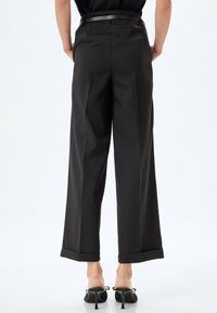 Pantaloni neri a vita alta con una vestibilità su misura, gambe larghe e orli arrotolati. Presentano una texture liscia e una sottile cintura nera in vita.