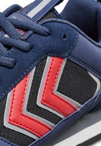 Navy athletic shoe featuring a textured upper with red and grey zigzag accents. Includes flat laces and a padded collar for comfort.