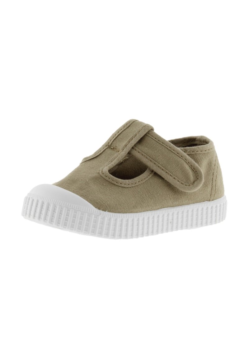 Zapato de lona color beige con cierre de cinta de velcro y punta redonda. Presenta una suela de goma blanca con textura estriada.