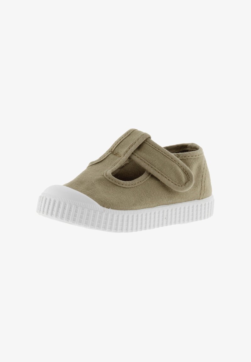 Zapato de lona color beige con cierre de cinta de velcro y punta redonda. Presenta una suela de goma blanca con textura estriada.