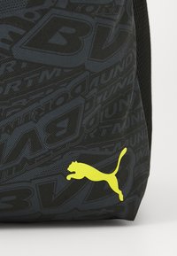 Schwarzer Stoff-Rucksack mit strukturiertem Muster; verfügt über ein gelbes Puma-Logo. Bietet Praktikabilität mit einem modernen, schlanken Design.