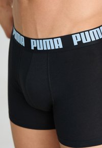 Boxeri negri din bumbac, cu un brâu elastic lat pe care este imprimat "PUMA" în albastru deschis. Vedere de aproape care arată potrivirea și textura.
