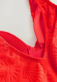 Costume da bagno rosso con tessuto testurizzato, caratterizzato da un profondo scollo a V, spalline regolabili e uno strato interno sovrapposto per supporto.