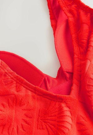 Röd simdräkt med texturerad tyg, med en djup V-ringning, justerbara axelremmar och ett inre lager för stöd.