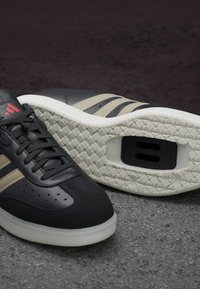 Czarne skórzane sneakersy z beżowymi paskami. Obejmują teksturowaną białą podeszwę oraz perforacje po bokach. Zawierają markowe akcenty.