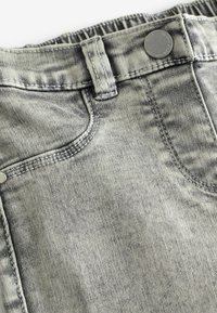 Grå denimjeans med en blekt tvätt, synlig sömnad, framfickor och knäppning. Elastisk midja för justerbar passform.