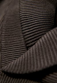 Dunkelbrauner, strukturierter Stoff mit vertikalen Rippungen, der sich durch sich überlappende Bereiche und ein weiches, plüschiges Aussehen auszeichnet.