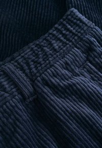 Námornícky rebrovaný materiál, mäkká textúra, s uvoľneným pásom. Pruhy sú vedené vertikálne cez materiál, čo pridáva hĺbku dizajnu.