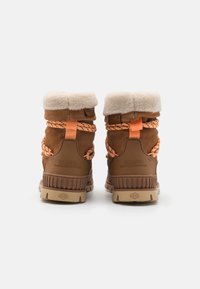 Brune semskede støvler med en fluffy beige krave, orange snørebånd og gummisåler med ribbet tekstur og branding på hælen.