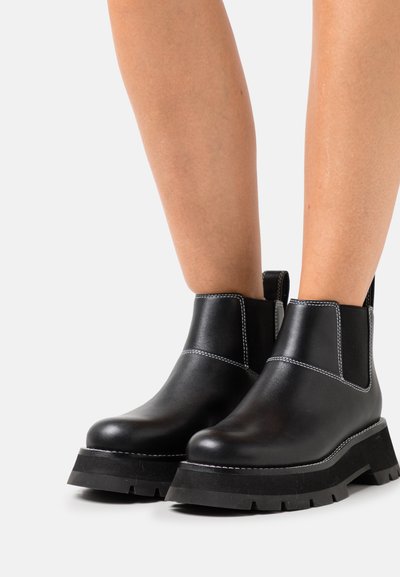 Μαύρες δερμάτινες μπότες μέχρι τον αστράγαλο με ελαστικές πλευρικές επενδύσεις, χοντρές καουτσούκ σόλες και λευκές ραφές. Απαλή υφή με ματ φινίρισμα.