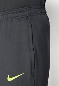 Melni sporta bikses ar elastīgu jostu, sānu kabatām un lielu neona zaļu Nike logotipu uz priekšpuses. Gluda, viegla auduma sastāvs.