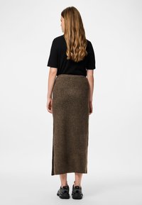 Jupe midi en tricot marron côtelé avec une fente haute, associée à un t-shirt noir et des chaussures de sport noires. Vue arrière de la tenue.